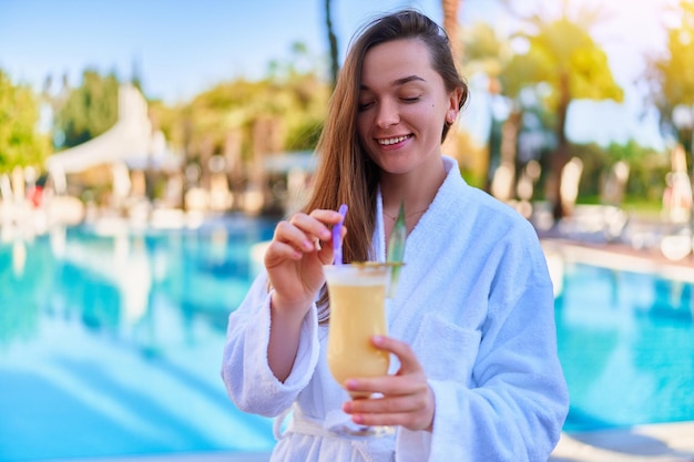 Une jeune femme souriante et heureuse profite de vacances d'été relaxantes avec un cocktail Pina colada rafraîchissant au bord de la piscine du complexe tout compris