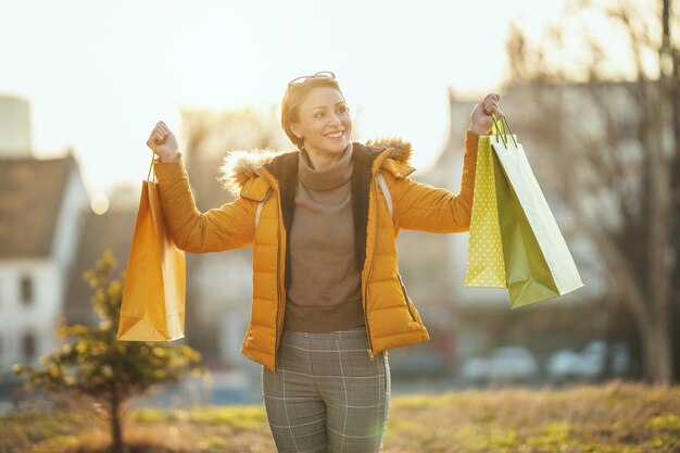 Une jeune femme souriante et heureuse se promène dans la rue d'une ville avec des sacs à provisions.