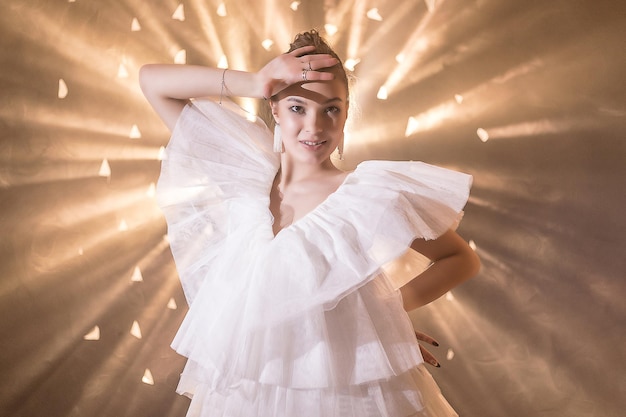 Une jeune femme souriante et heureuse vêtue d'une robe blanche pose dans les rayons des projecteurs et dans la fumée d'une machine à fuméeConcept mariée ballerine dansebonheur
