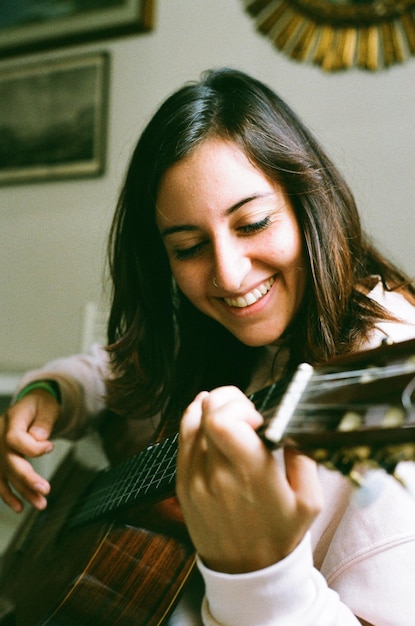 Une jeune femme souriante jouant de la guitare assise à la maison.