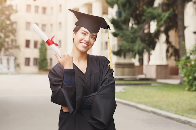 Jeune femme souriante le jour de sa remise des diplômes à l'université titulaire d'un diplôme. Concept d'éducation, de qualification et de robe.