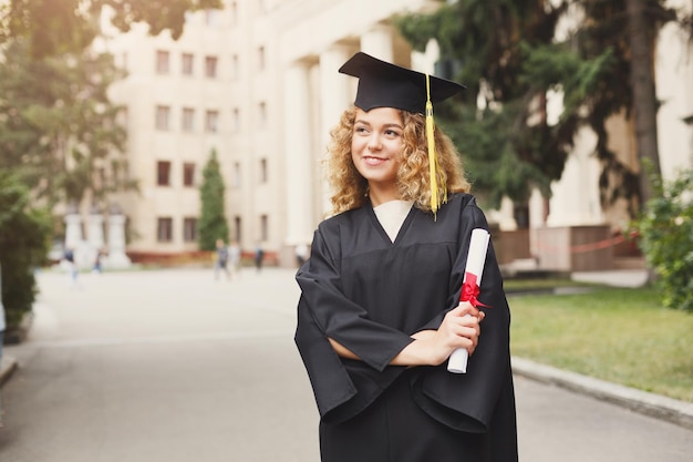 Jeune femme souriante le jour de sa remise des diplômes à l'université titulaire d'un diplôme. Concept d'éducation, de qualification et de robe.