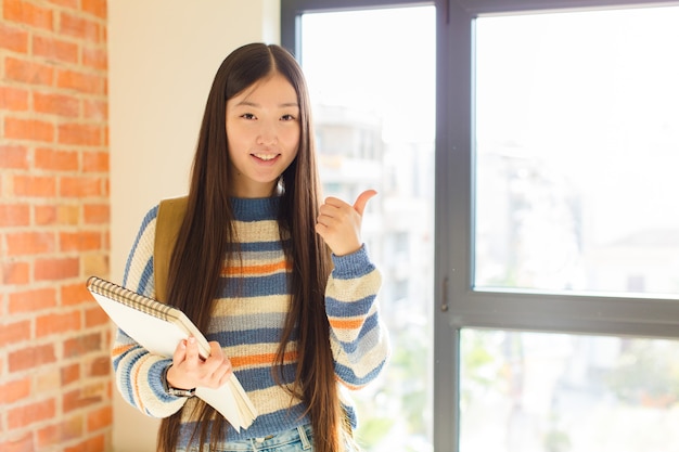 Jeune femme souriante joyeusement et à la recherche de bonheur, se sentir insouciant et positif avec les deux pouces vers le haut