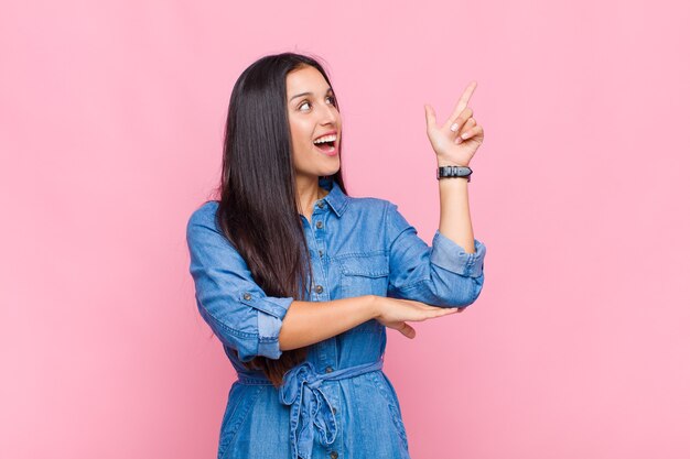 Jeune femme souriante joyeusement et regardant de côté, se demandant, pensant ou ayant une idée