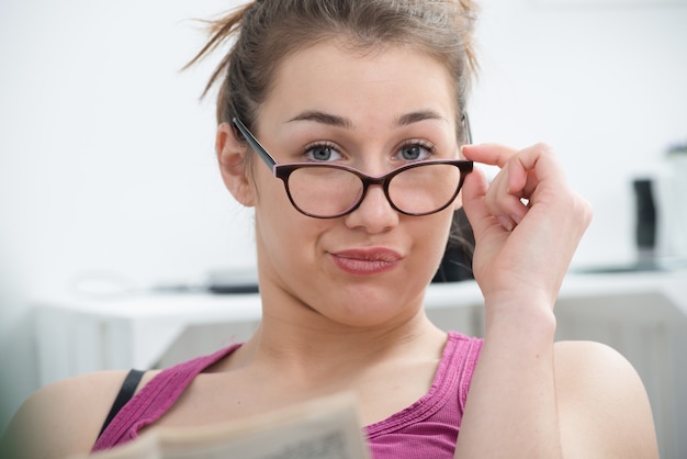 Jeune femme souriante avec des lunettes, lisant le journal