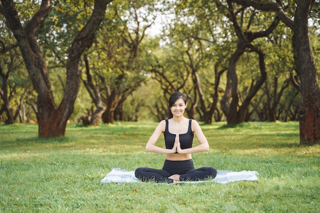 Jeune femme souriante méditant en position du lotus assis sur l'herbe dans le parc. Concept de yoga et d'harmonie.