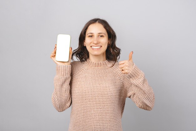 Jeune femme souriante montre un écran vide et le pouce vers le haut