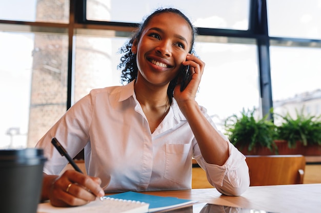 Photo jeune femme souriante parlant sur smartphone au café