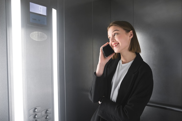 Jeune femme souriante parle par son smartphone dans l'ascenseur.