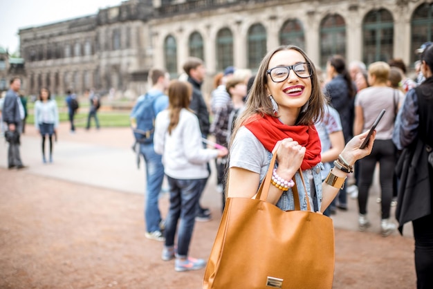 Jeune femme souriante photographiant avec un smartphone lors d'une visite avec un groupe de touristes l'ancien palais de la ville de Dresde, Allemagne