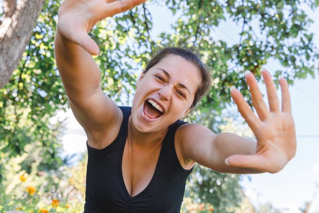 Jeune femme souriante en plein air. Belle fille brune au repos sur fond vert parc ou jardin. Femme heureuse gratuite à l'heure d'été. Concept de personnes heureuses insouciantes de bonheur de liberté.