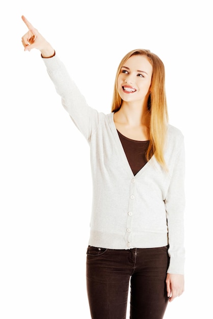 Une jeune femme souriante pointant contre un fond blanc.