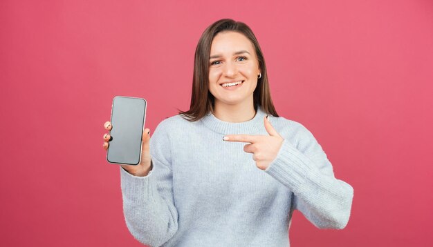 Jeune femme souriante pointe vers le téléphone qu'elle tient dans un studio