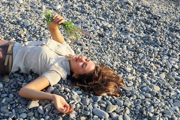 Jeune femme souriante portant sur des galets et détient un petit bouquet de fleurs sauvages