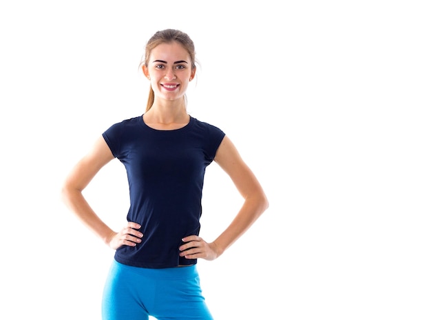 Jeune femme souriante portant un T-shirt bleu et des leggings debout sur fond blanc en studio