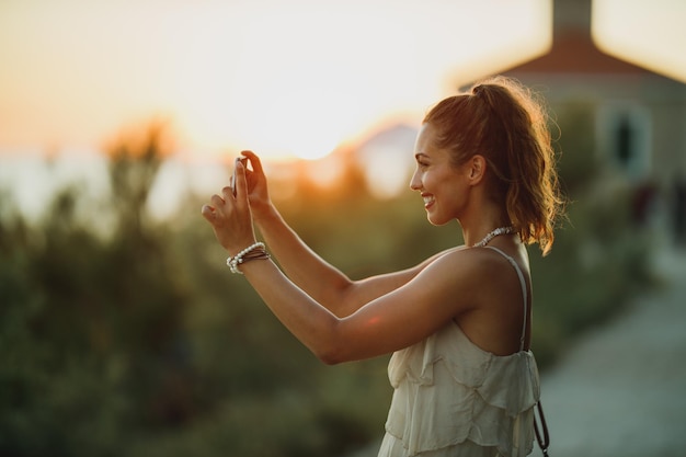 Une jeune femme souriante prenant des photos avec son smartphone tout en profitant des vacances d'été.