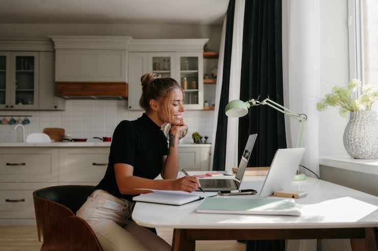 Photo une jeune femme souriante prend des notes et regarde l'ordinateur portable alors qu'elle travaille à la maison