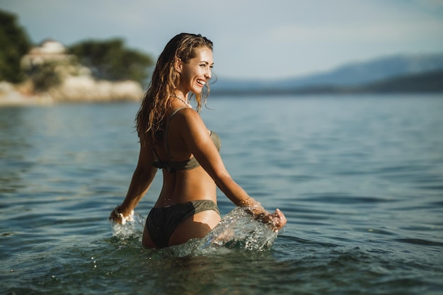 Une jeune femme souriante profitant de la plage et se relaxant dans l'eau de mer.