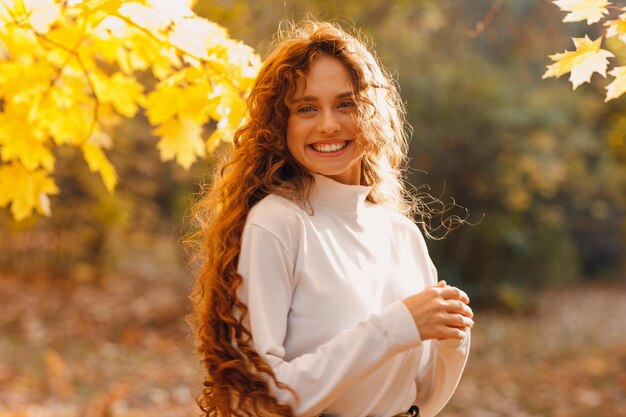 Une jeune femme souriante profite du temps d'automne dans le parc avec les feuilles jaunes sur les branches