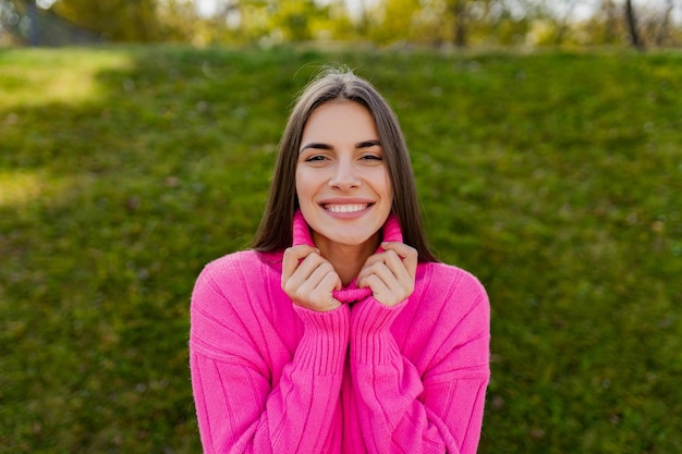 Jeune femme souriante en pull rose marchant dans un parc verdoyant