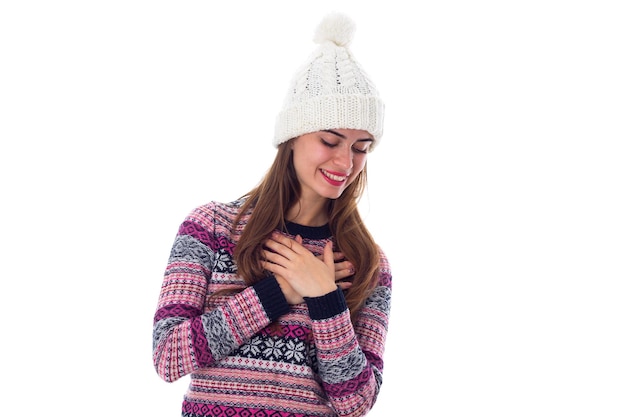 Jeune femme souriante en pull violet et chapeau blanc regardant vers le bas sur fond blanc en studio