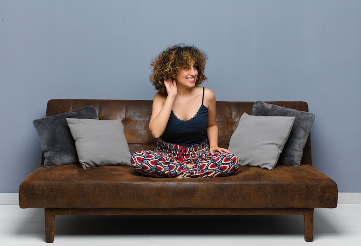 Photo jeune femme souriante, regardant curieusement sur le côté, essayant d'écouter des commérages ou d'entendre un secret assis sur un canapé.