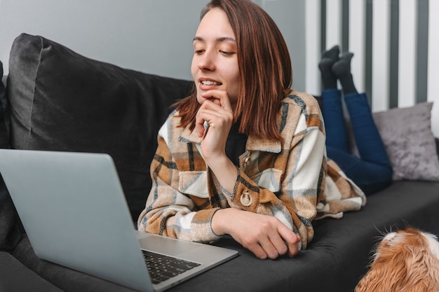 Jeune femme souriante regardant un ordinateur portable en position allongée sur un canapé à la maison