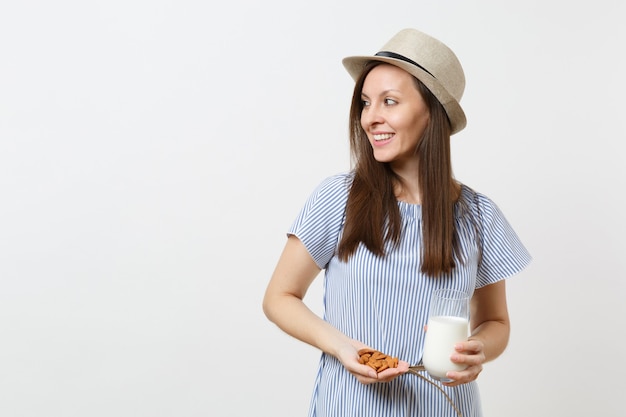 Une jeune femme souriante regarde de côté, tient dans les mains Lait d'amande en verre, noix d'amande isolées sur fond blanc. Une bonne nutrition, une boisson végétarienne végétalienne, un mode de vie sain, un concept de régime. Espace de copie.