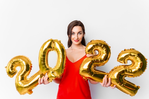 Jeune femme souriante en robe de cocktail rouge avec un maquillage lumineux célébrant le nouvel an et tenant de l'or...