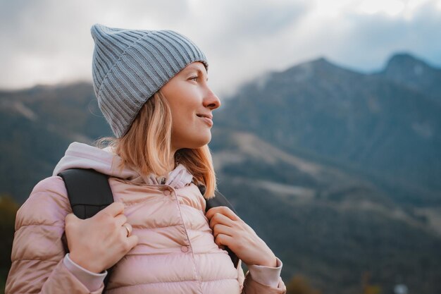 Jeune femme souriante avec un sac à dos dans un chapeau admirant regarde les montagnes