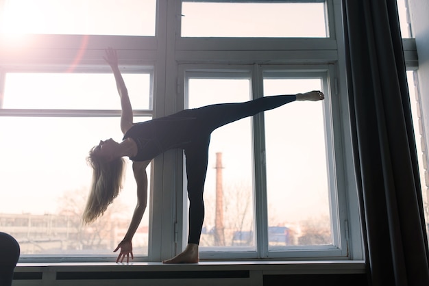 Jeune femme souriante séduisante pratiquant le yoga, faisant de l'exercice, portant des vêtements de sport, un soutien-gorge, un entraînement à domicile