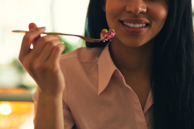 Jeune femme souriante avec ses dents révélées et tenant de la nourriture sur la fourchette près de sa bouche