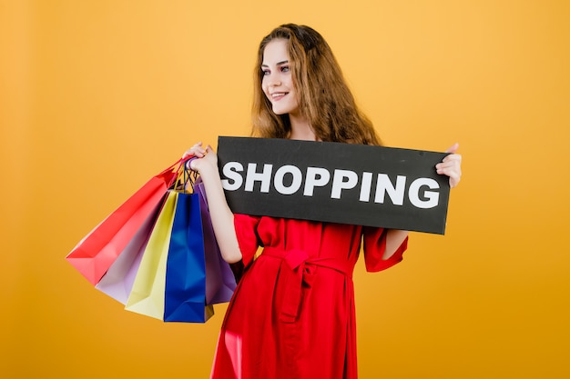 Jeune femme souriante avec signe de shopping et sacs à provisions colorés isolés sur jaune