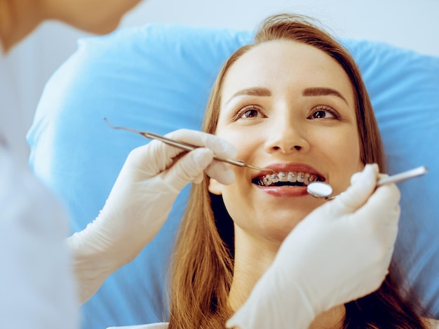 Une jeune femme souriante avec des supports orthodontiques examinée par un dentiste dans une clinique dentaire.