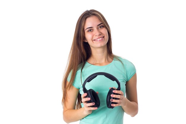 Jeune femme souriante en T-shirt bleu tenant un casque noir sur fond blanc en studio