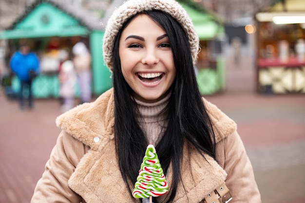 Jeune femme souriante et tenant des bonbons en se tenant à la foire des vacances d'hiver