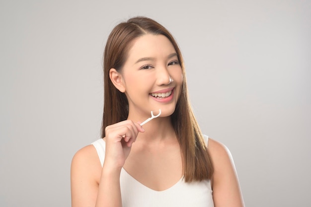 Jeune femme souriante tenant du fil dentaire sur fond blanc studio