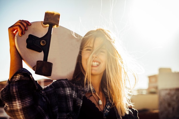 Une jeune femme souriante tenant un skateboard contre le ciel