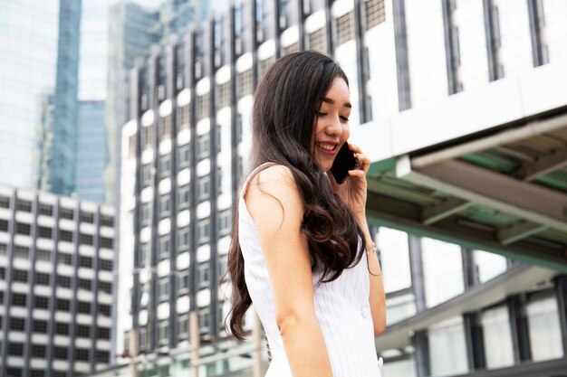 Une jeune femme souriante tenant un téléphone portable alors qu'elle se tient dans la ville