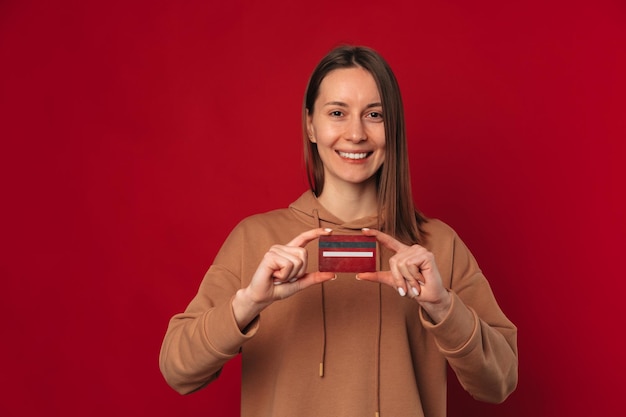 Jeune femme souriante tient une carte de crédit rouge devant sa poitrine