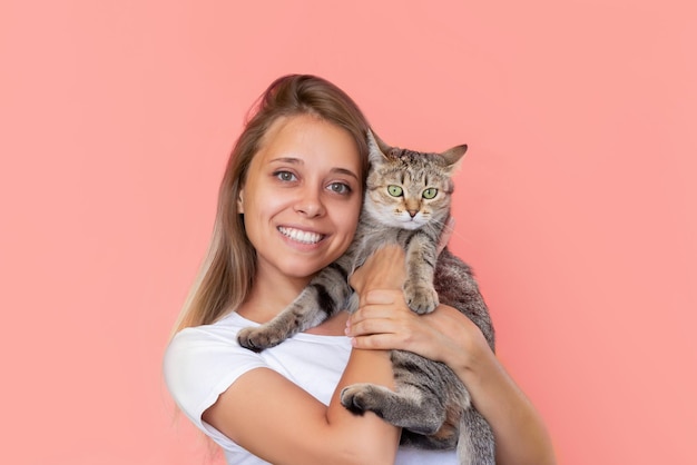 Une jeune femme souriante tient un jeune chat tigré dans ses mains isolées sur fond rose couleur