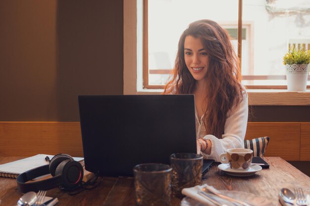 Une jeune femme souriante et travaillant dans un restaurant avec son ordinateur portable