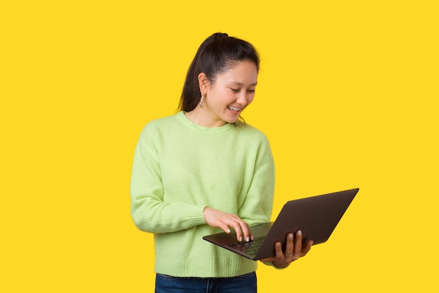 Jeune femme souriante utilise un ordinateur portable en se tenant debout sur jaune.