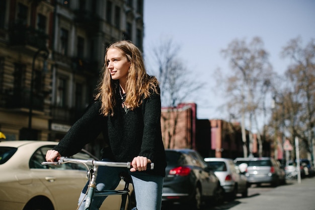 Une jeune femme souriante avec un vélo dans la rue de la ville