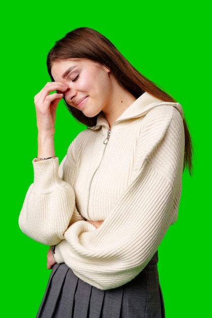 Une jeune femme souriante avec les yeux fermés debout sur un fond vert