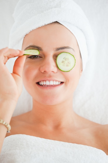 Jeune femme avec un sourire entendu avec des tranches de concombre sur le visage