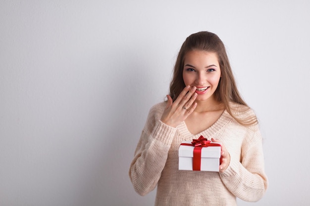 Jeune femme sourire heureux tenir la boîte-cadeau en mains debout sur fond gris