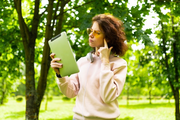 Jeune femme avec un sourire parfait, tient une tablette dans les mains et pense