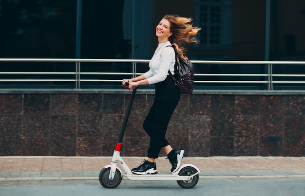 Jeune femme avec sourire ride scooter électrique dans la rue