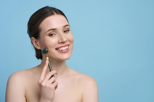 une jeune femme sourit en regardant la caméra effectue un drainage lymphatique ou un massage de lifting du visage